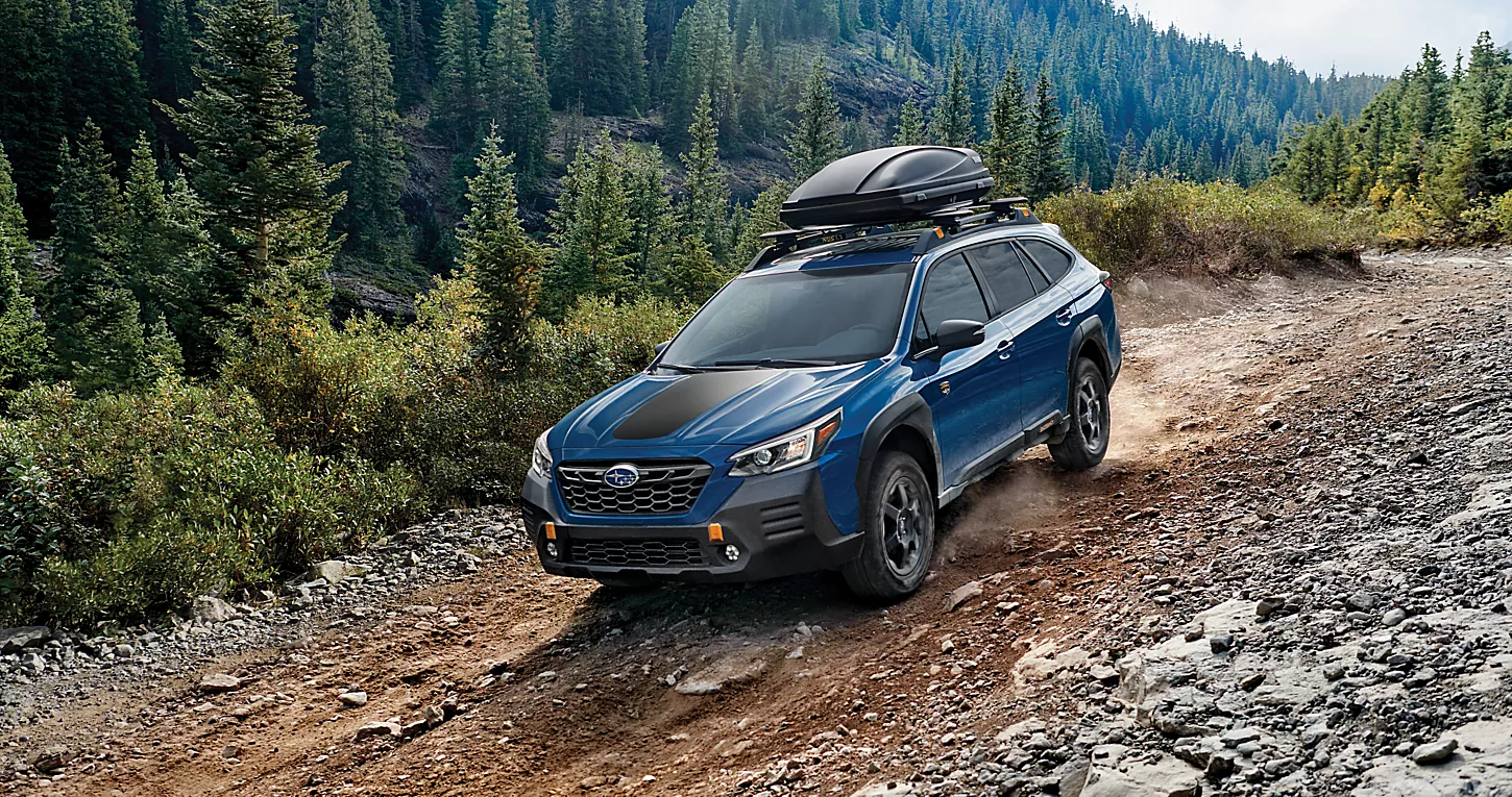 2023 Subaru Outback driving down a dirt road, surrounded by trees