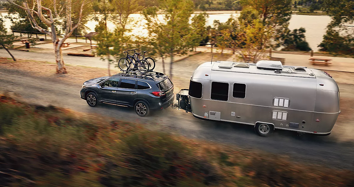Magnetite Gray Metallic 2024 Subaru Ascent towing a metal retro camper with two bikes on the bike rack on gravel road