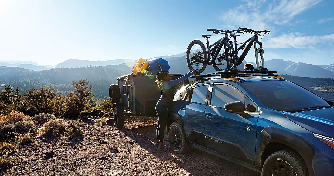  2024 Blue Subaru crosstrek wilderness towing a large camper and two bikes on the top bike rack.