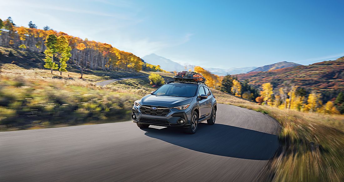 2024 Subaru Crosstrek driving on winding road with mountains and trees in background