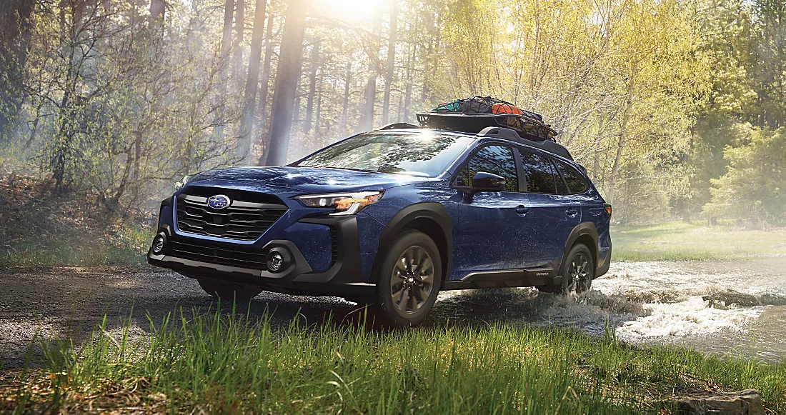 2024 Dark Blue Subaru outback wilderness driving through a rugged forest terrain with camping gear on the top rack