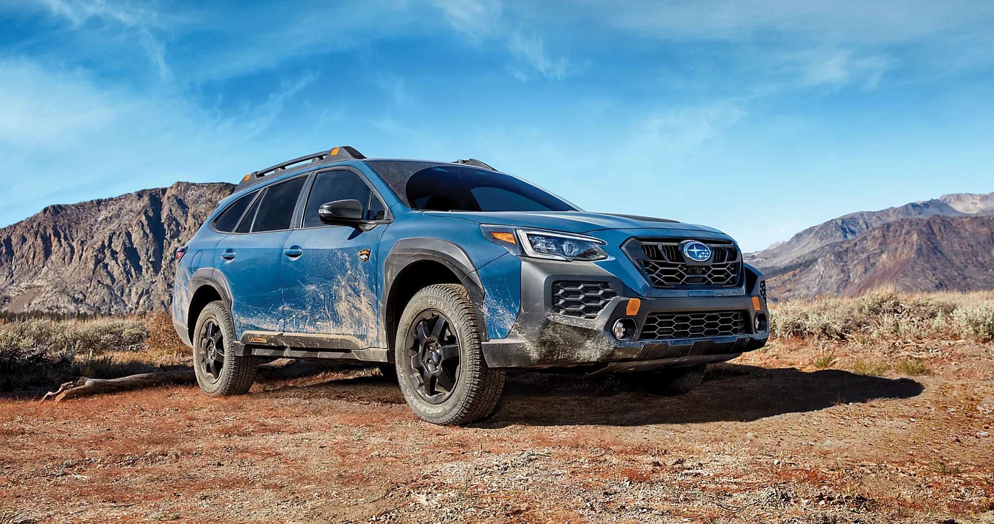  Geyser blue Subaru wilderness outback covered in dirt parked on dry desert terrain 