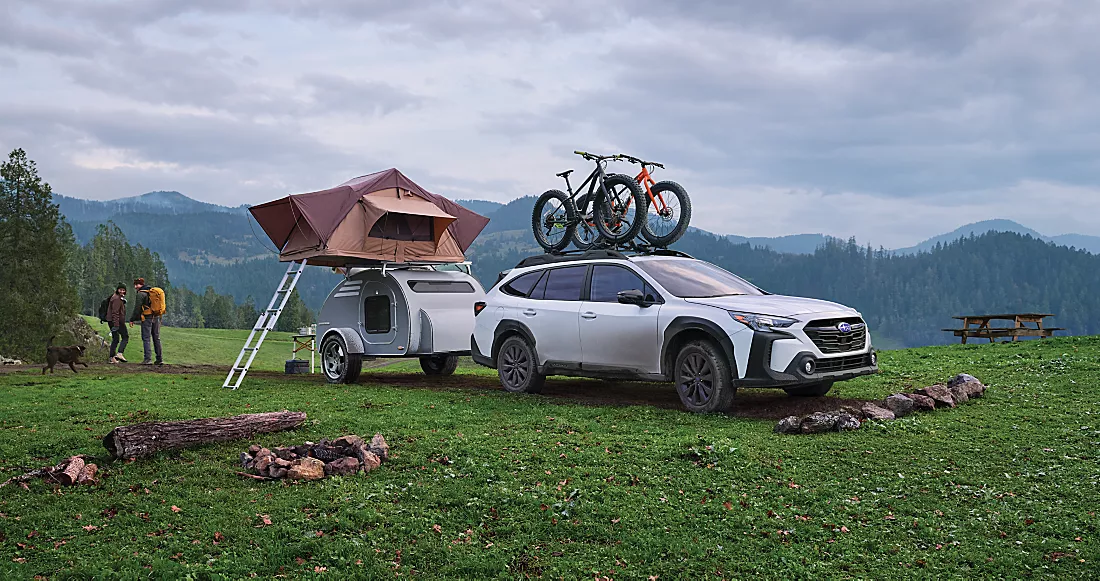  White 2024 Subaru outback towing a camper and two large bikes on the bike rack 