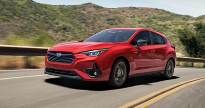A red Subaru Impreza hatchback drives on a country highway