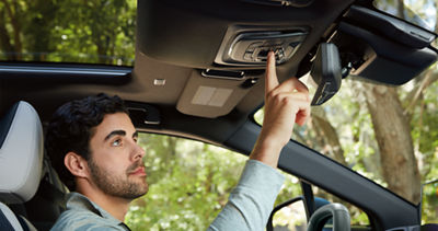 A man presses a Subaru Connected Services button on the roof of his vehicle.