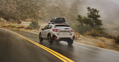 2026 Crosstrek Hybrid SUV with storage on roof rack driving down winding mountain roads.