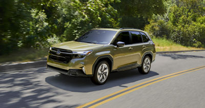 A 2026 Subaru Forester Hybrid AWD SUV driving on a road in a treelined area.