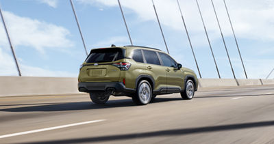 A 2026 Subaru Forester Hybrid in Autumn Green Metallic drives across a suspension bridge.