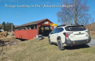 A white Subaru Outback parked in front of a covered bridge