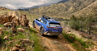 2026 Subaru EV SUV driving up a steep, rocky incline
