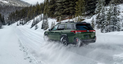 A green 2026 Outback driving through the snow.