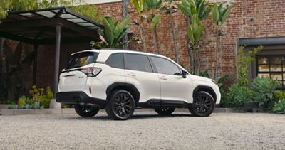 White Subaru Forester Sport Onyx parked on gravel road near brick building with greenery.