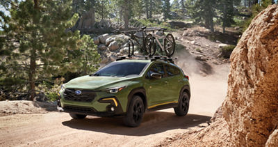 A green Subaru Crosstrek drives through a ravine with two bicycles on its roof rack