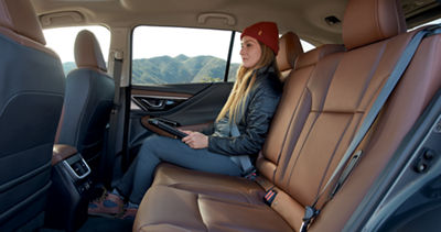 A woman sitting in the backseat of a Subaru Outback midsize SUV