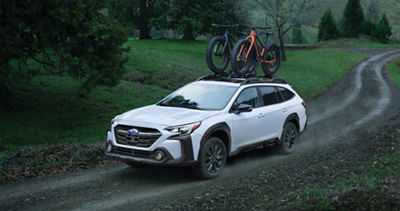 A white Subaru Outback midsize SUV carries two bicycles on its roof