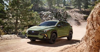 A green Subaru Crosstrek drives through a ravine with two bicycles on its roof rack. 