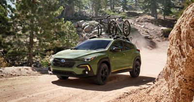 A green Subaru Crosstrek drives through a ravine with two bicycles on its roof rack.
