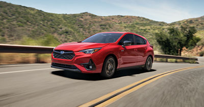 A red Subaru Impreza hatchback drives on a country highway.