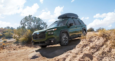 A green Subaru Outback midsize SUV navigates through a mountain pass. 