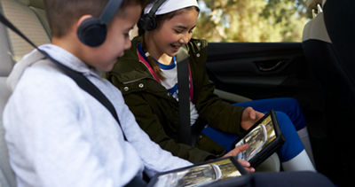 Two children wearing headphones using tablets in the backseat of a Subaru Ascent.