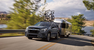 An Ascent full-size SUV with two bicycles on its roof rack tows a silver camper.