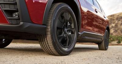 / Primer plano trasero de las ruedas y neumáticos de un Subaru Ascent 2026 color rojo estacionado en el desierto. 