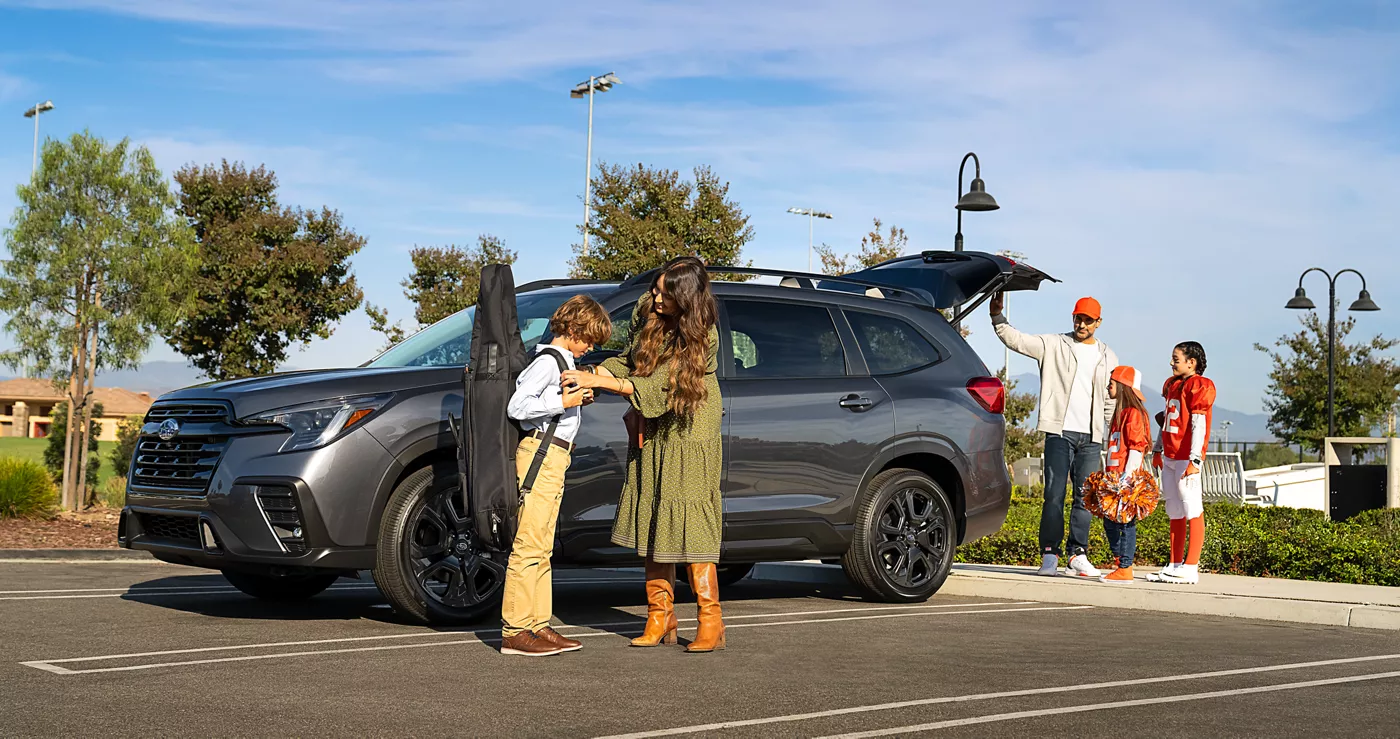 A grey Subaru Ascent parked at a beach lot as a group unloads surfboards