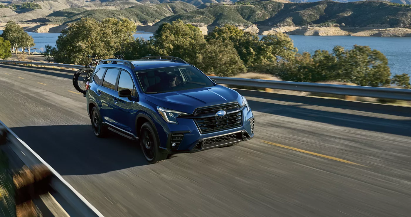 A blue Subaru Ascent on a coastal road above a reservoir