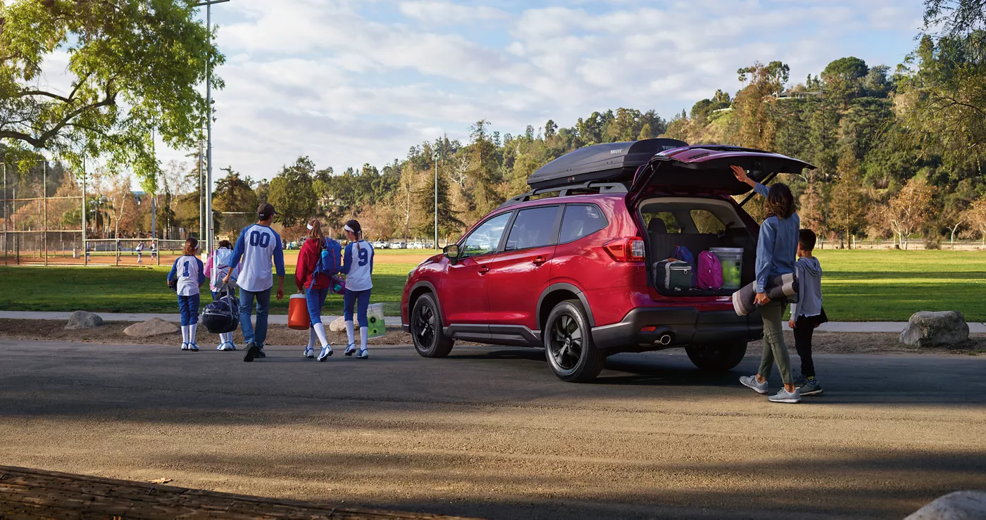 A red Subaru Ascent with its rear gate open at a park as a youth team walks past