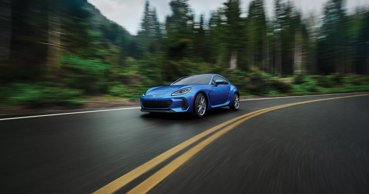 A blue Subaru BRZ on a forest road
