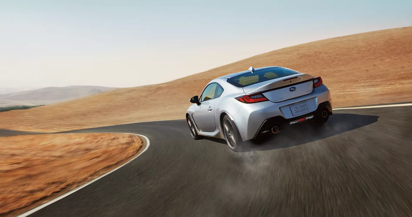 A silver Subaru BRZ on a curve through golden hills
