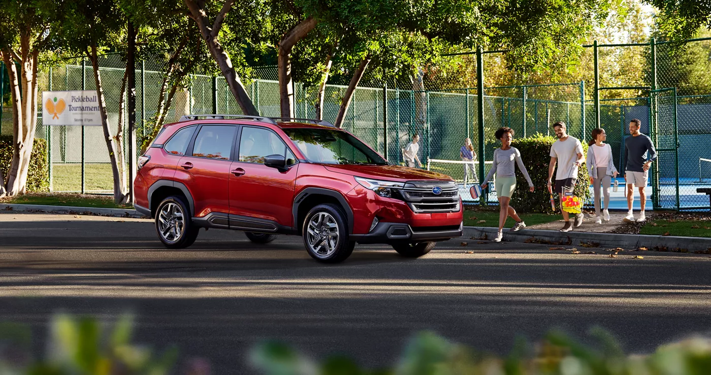 A red Subaru Forester parked by a tennis court as players walk past