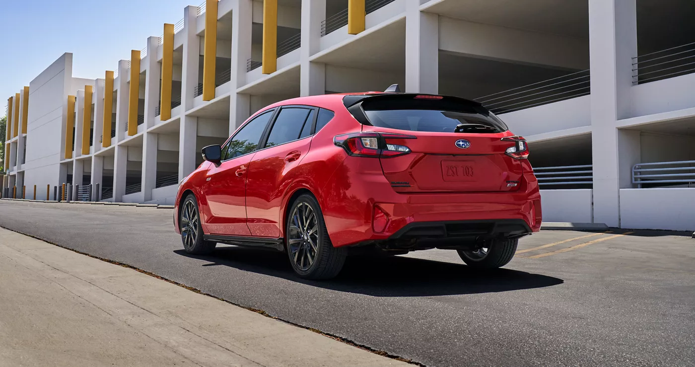 A red Subaru Impreza parked beside a concrete parking structure