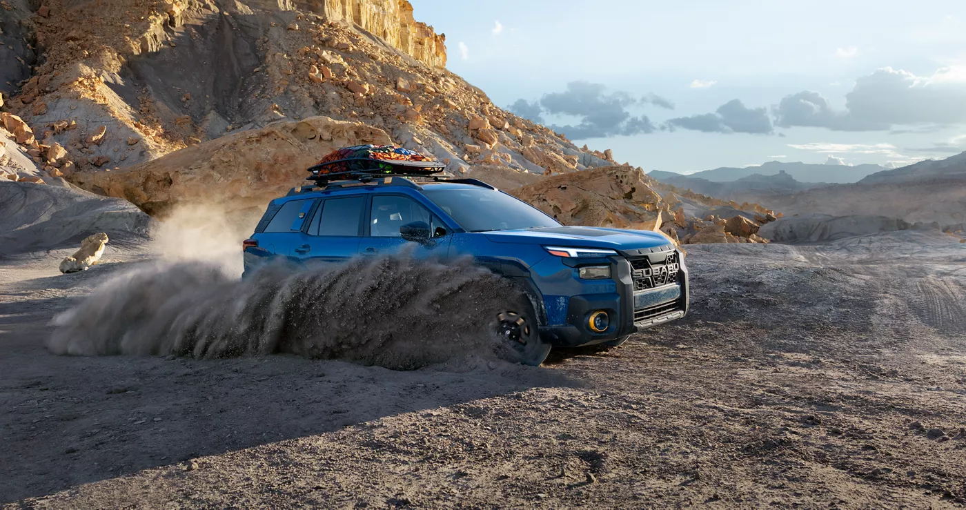 A blue Subaru Outback Wilderness splashing through water