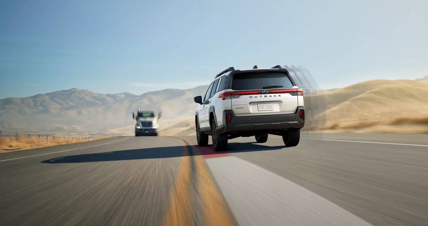 A white Subaru Outback on a desert highway, seen from behind