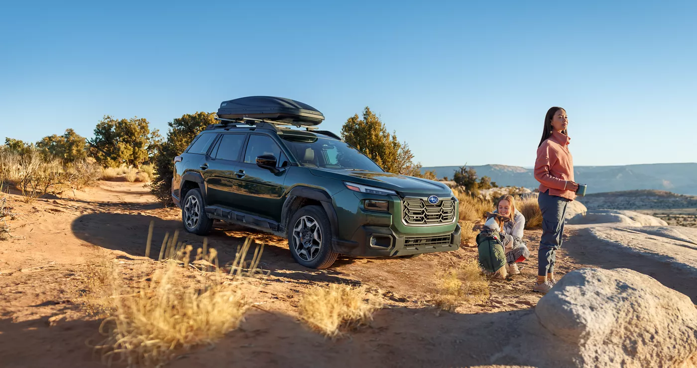 A green Subaru Outback parked at a desert overlook with a family