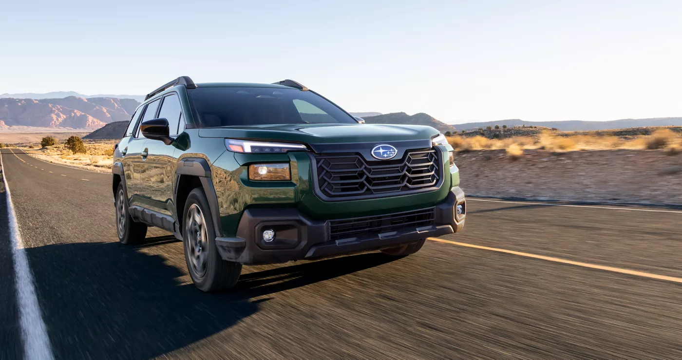 A green Subaru Outback on an open desert road