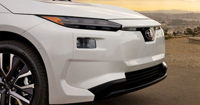 Side view of the front bumper of a white 2026 Subaru Solterra, showing off the headlights, and Subaru logo.