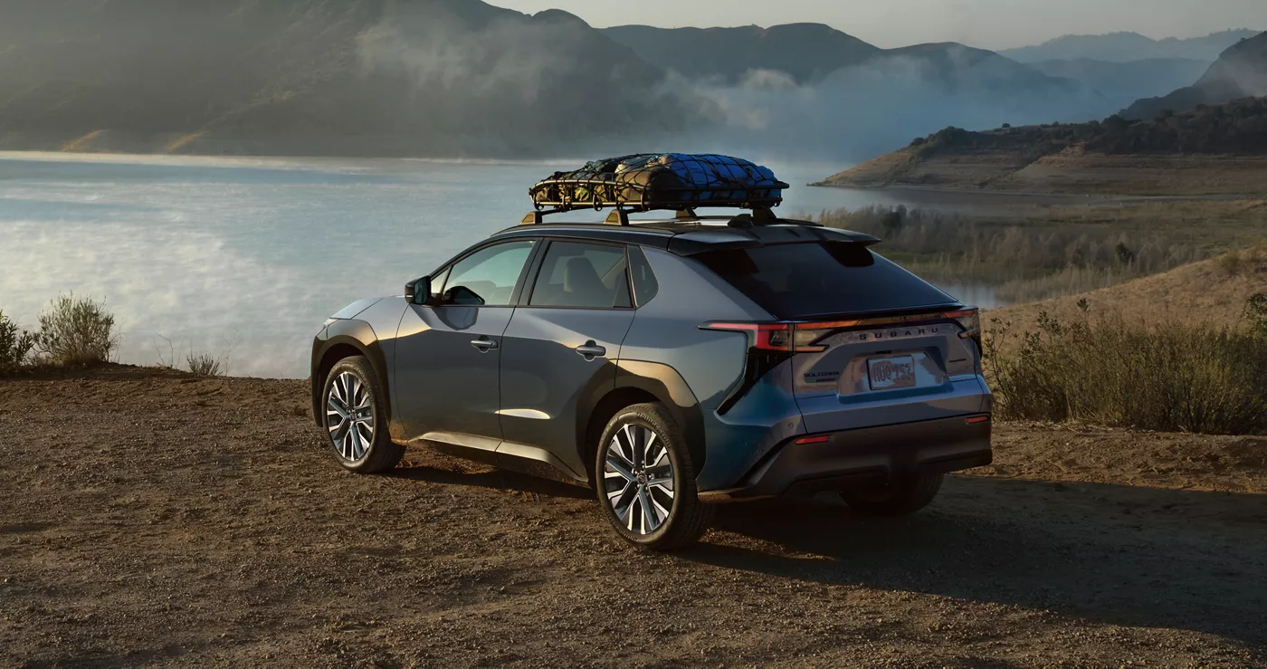 A Subaru Solterra with roof gear parked above a coastal lake