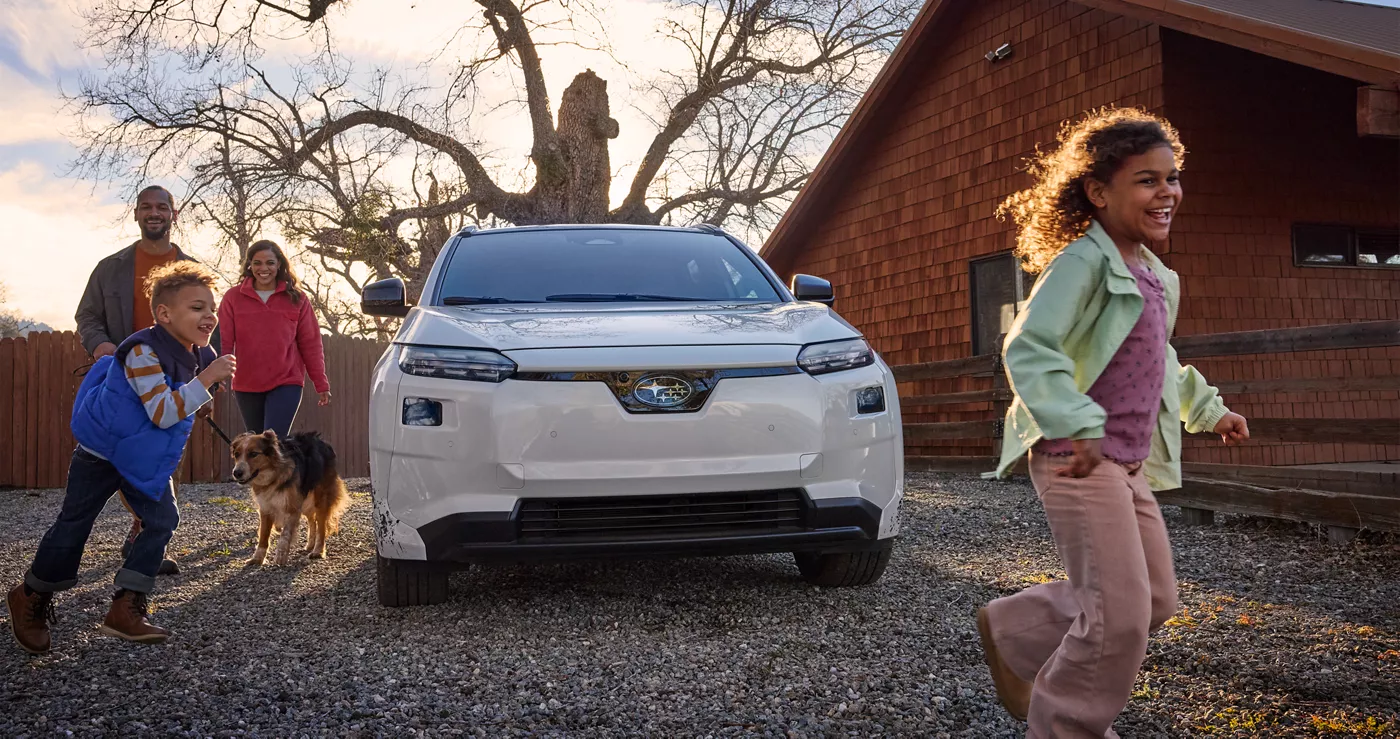 A white Subaru Solterra parked at a house as a family walks up