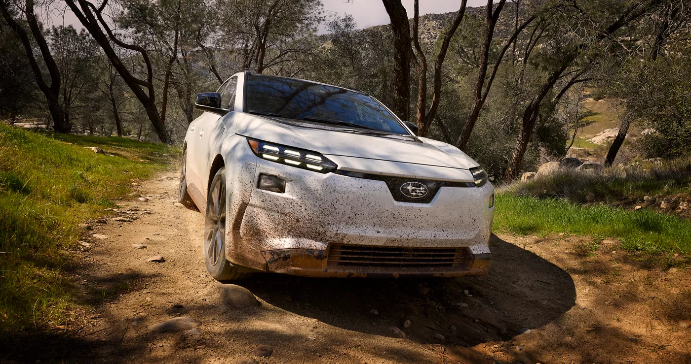A white Subaru Solterra on a dirt trail among trees