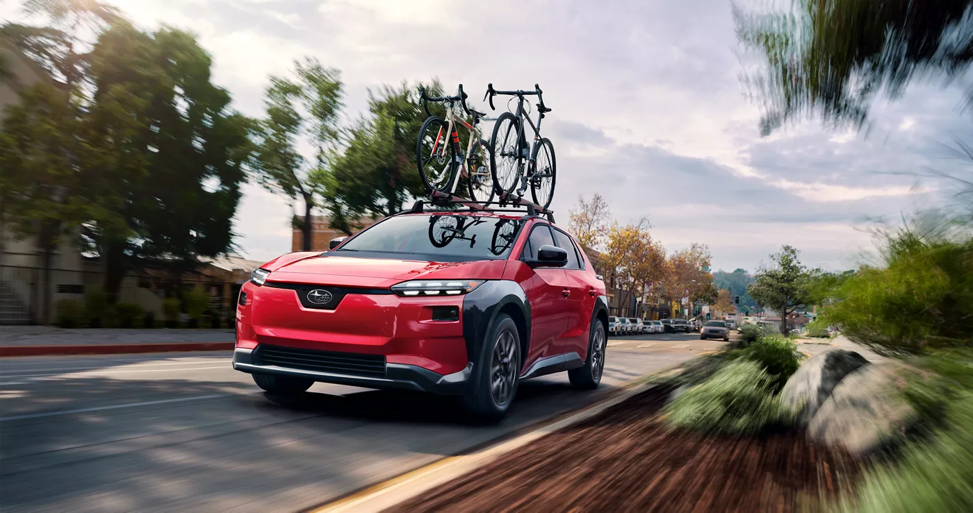 A red Subaru Solterra carrying bikes through a neighborhood