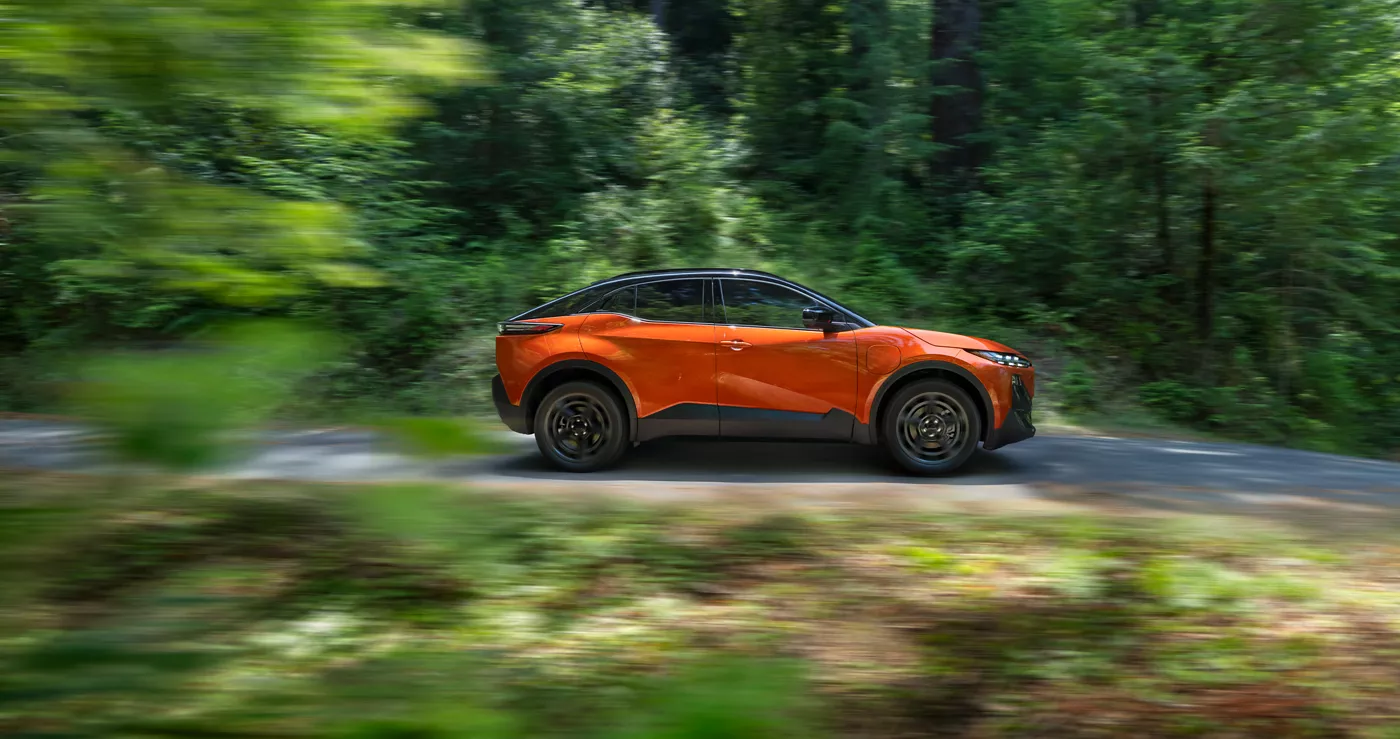An orange Subaru Uncharted in profile past dense greenery