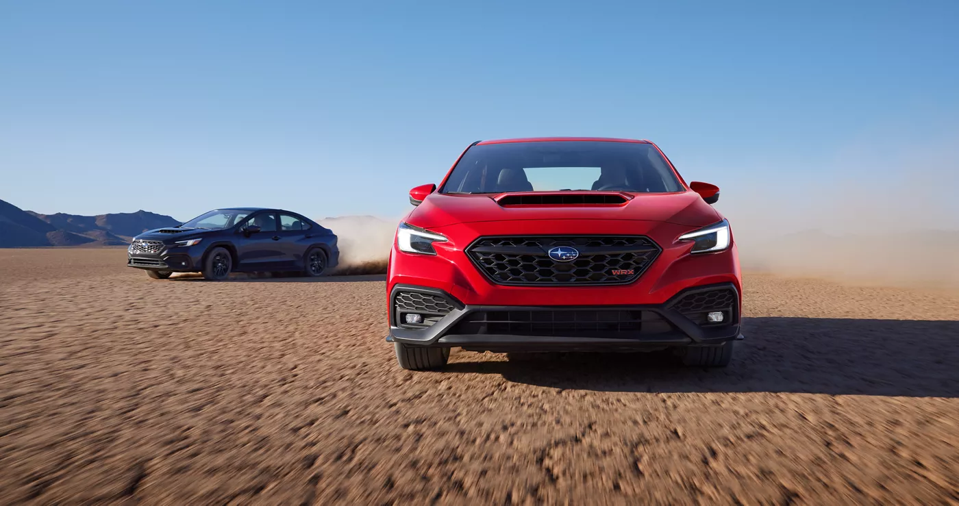 A red and a blue Subaru WRX parked on a dry lake bed