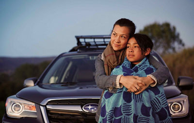 Woman hugging child who is wrapped up in a towel in front of black car.
