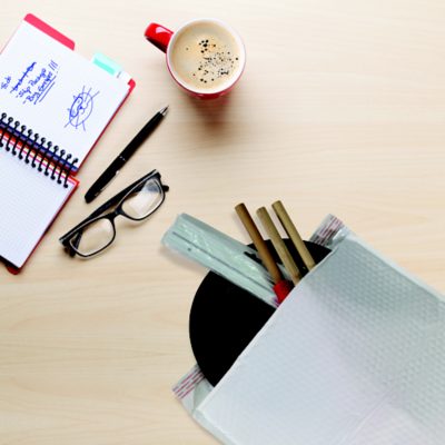 Jiffy Tuffgard mailer, glasses, coffee, and a notepad on a wood desk