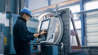 Factory worker programming a machine with a tablet computer.