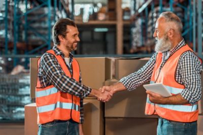 Two warehouse technicians smiling and shaking hands