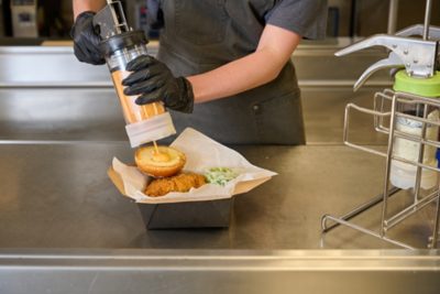 food service worker using flexprep dispenser to squirt a condiment onto a hamburger roll