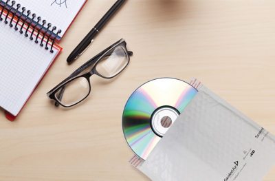 desk with a CD packed in a Jiffy Tuffgard mailer, glasses, pen, and notebook